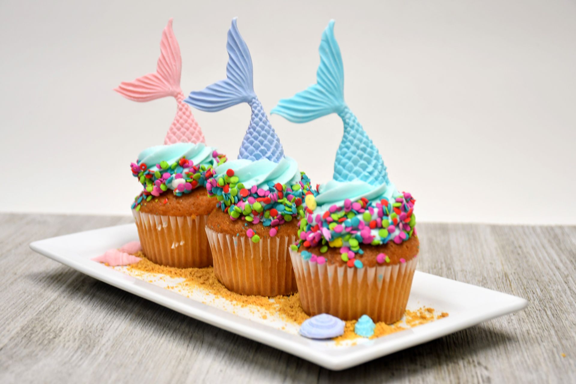 Three mermaid tail cupcakes with sprinkles on a white plate.