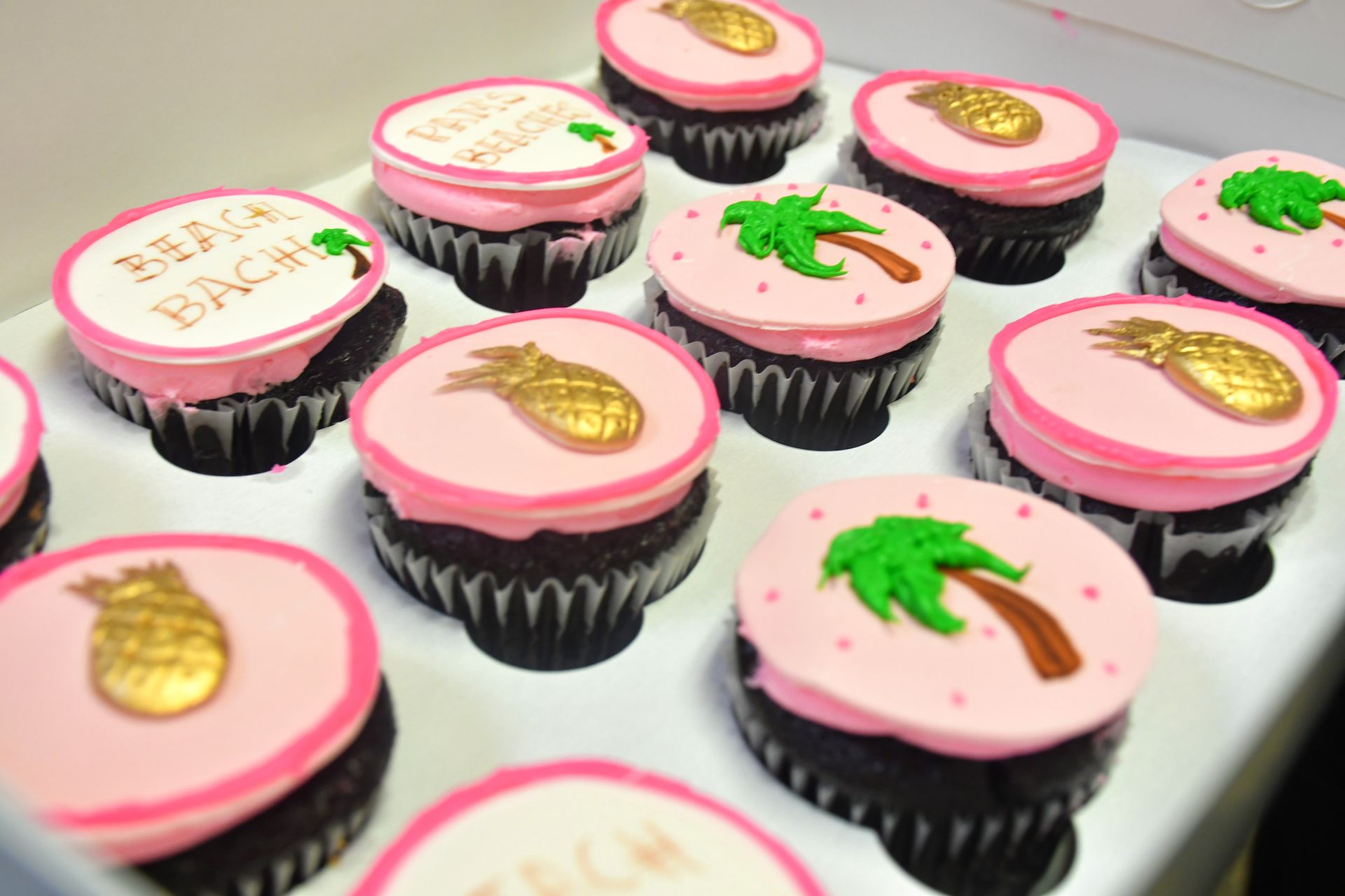 A box of cupcakes with pink frosting and pineapples on them