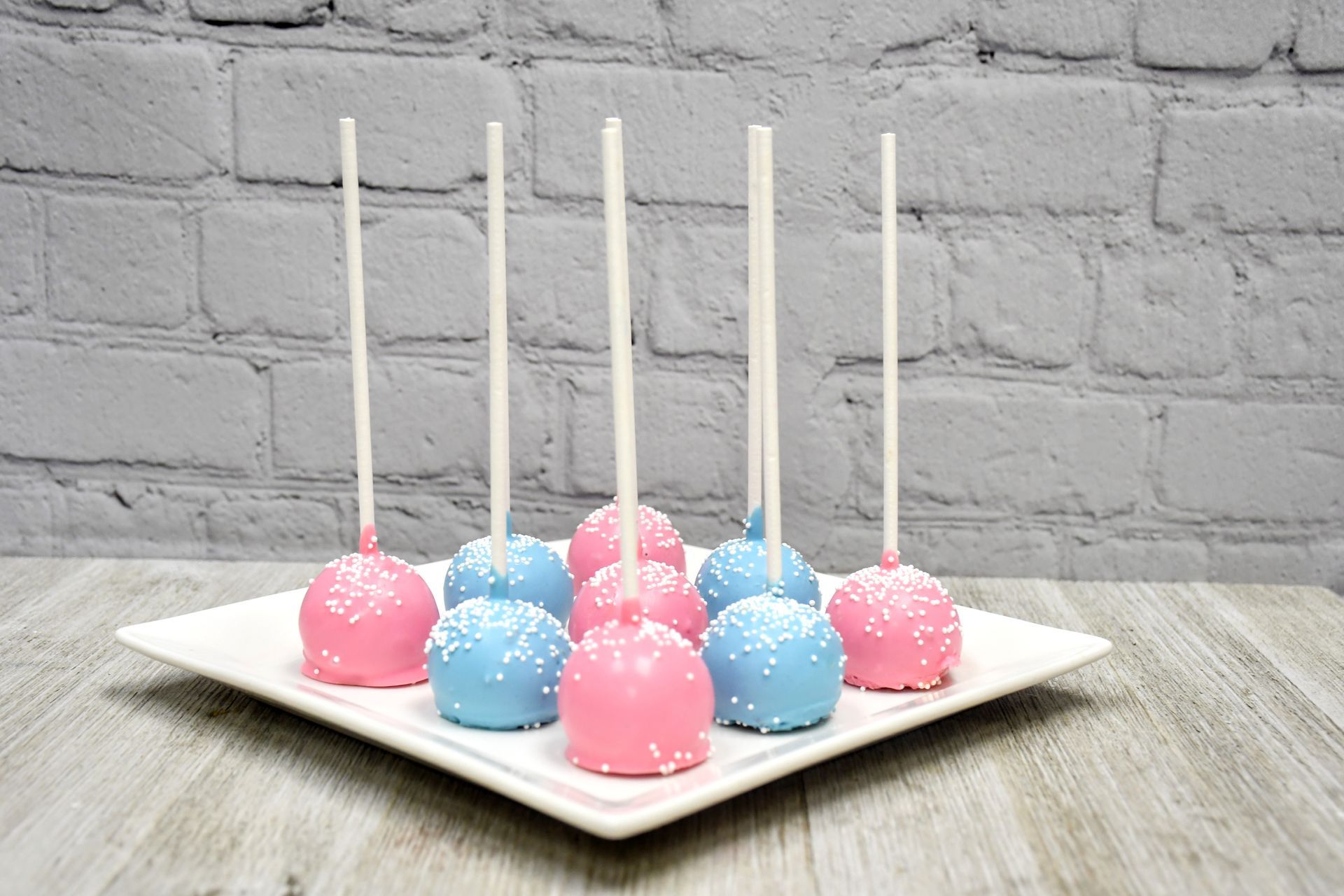 A white plate topped with pink and blue cake pops on sticks.