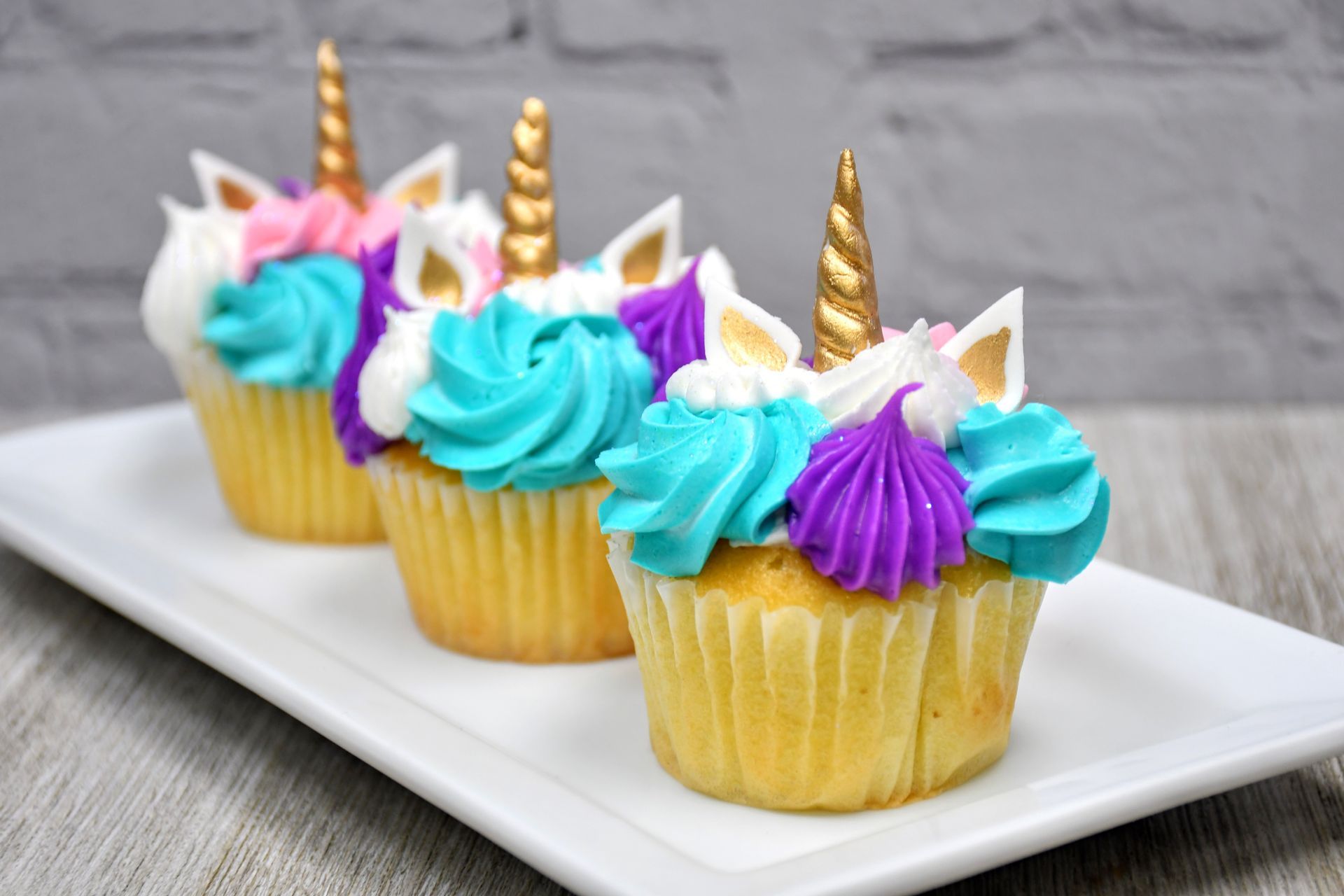 Three cupcakes decorated to look like unicorns are sitting on a white plate.