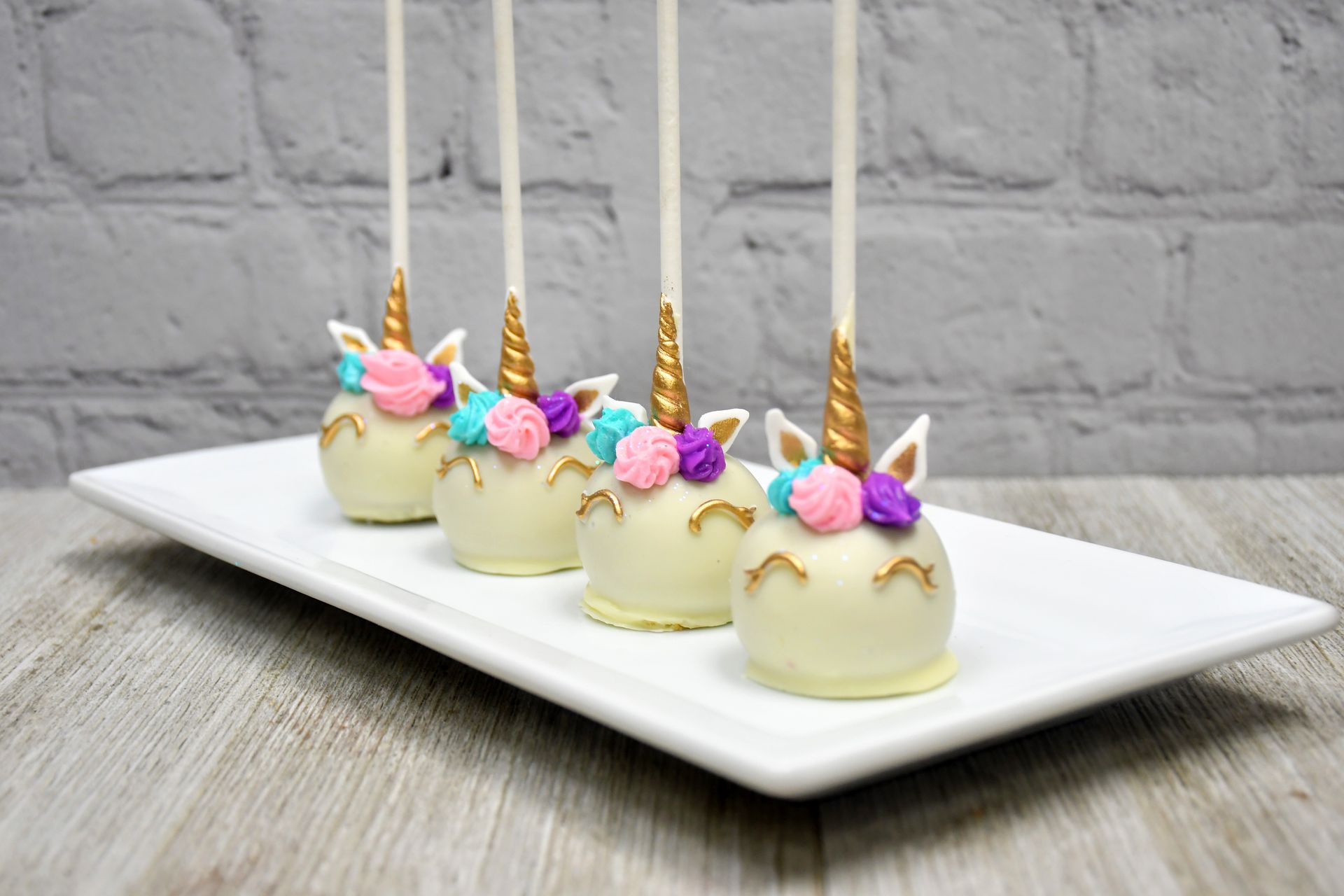 A row of unicorn cake pops on a white plate.