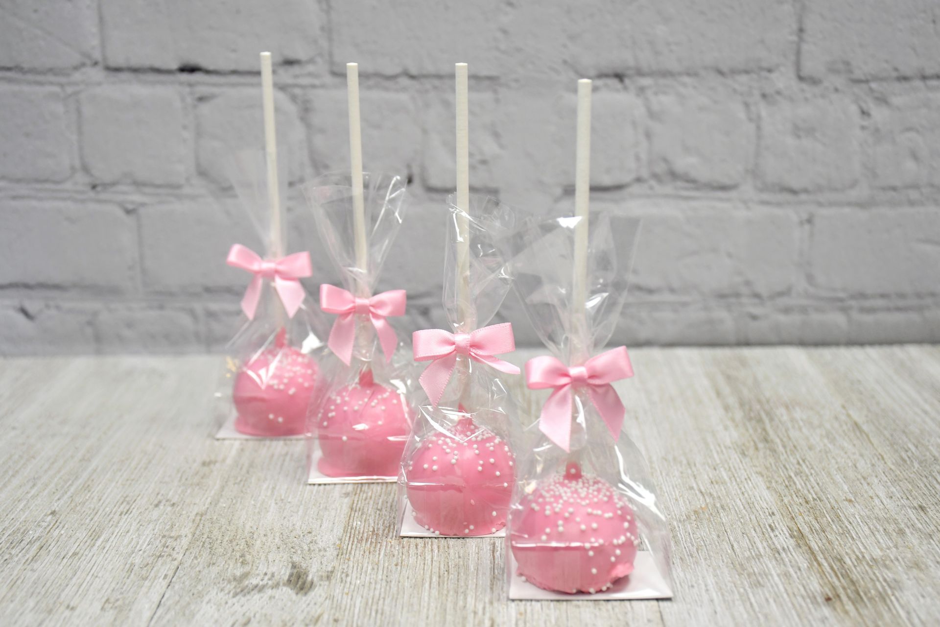 A row of pink cake pops with pink bows on a wooden table.