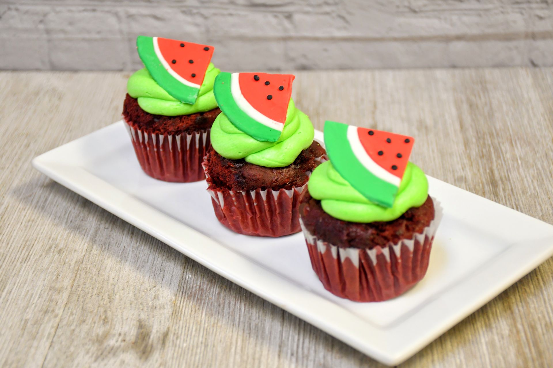 Three watermelon cupcakes with green frosting on a white plate.