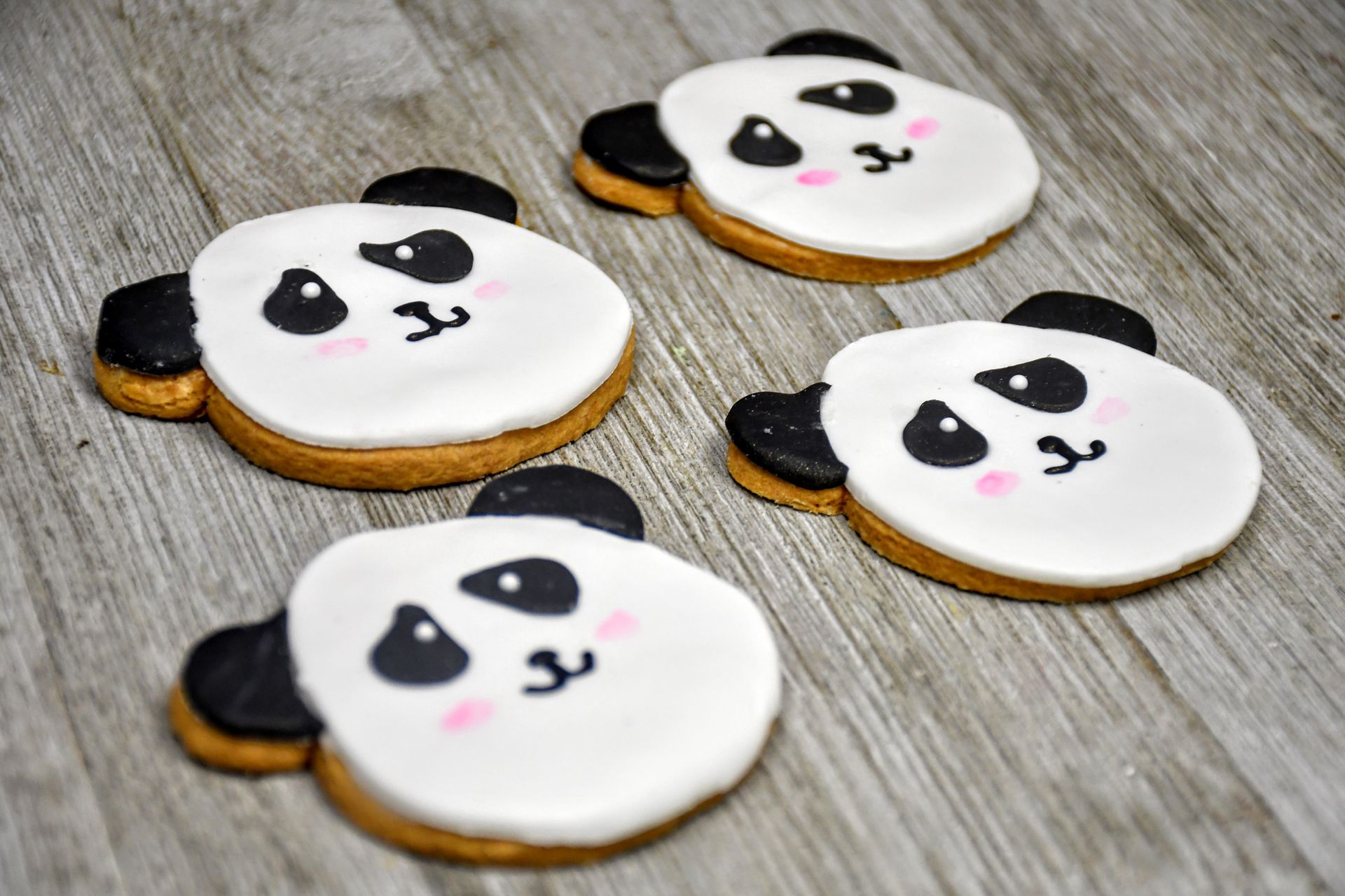 Four panda bear cookies are sitting on a wooden table.