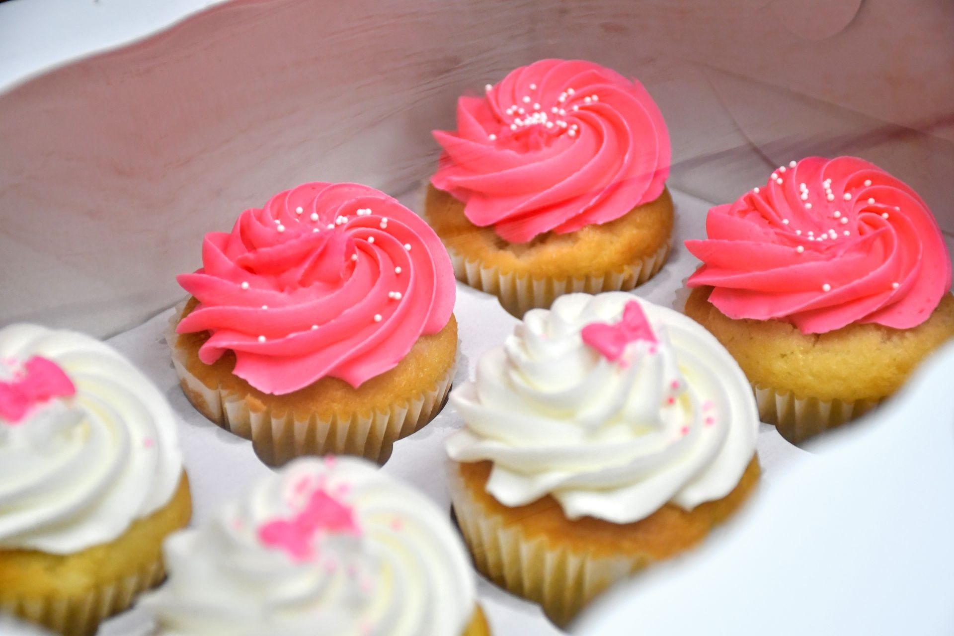 A box of cupcakes with pink frosting and white frosting