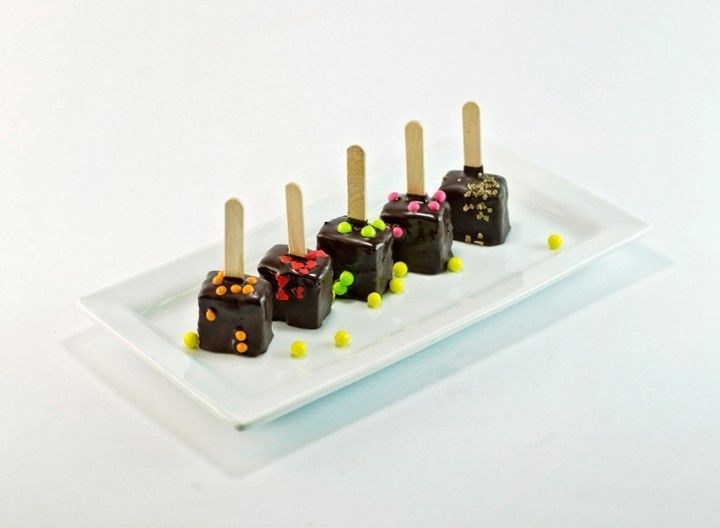 A white plate topped with chocolate covered popsicles and sprinkles.