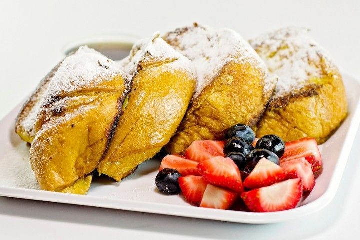 French toast with powdered sugar and strawberries and blueberries on a white plate.