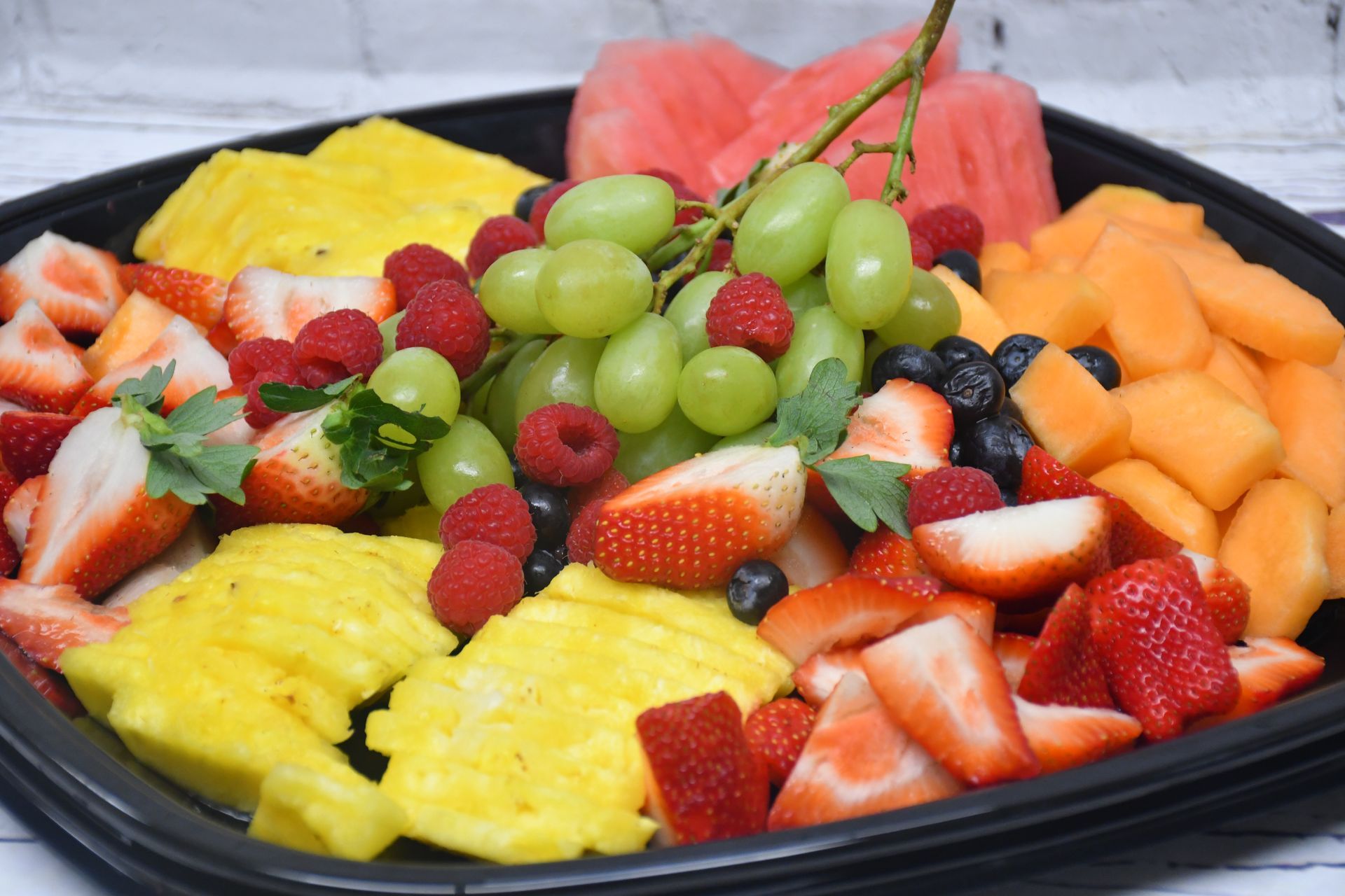 A tray of fruit including pineapple , strawberries , grapes , raspberries and melon.