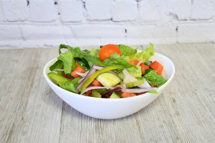 A salad in a white bowl on a wooden table.