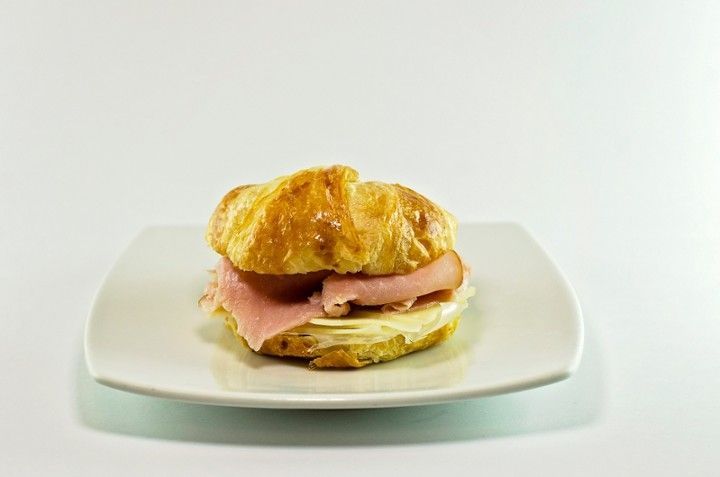 A ham and cheese sandwich on a croissant on a white plate.