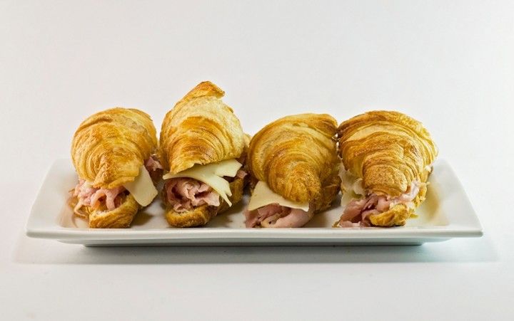 Four croissants with ham and cheese on a white plate.