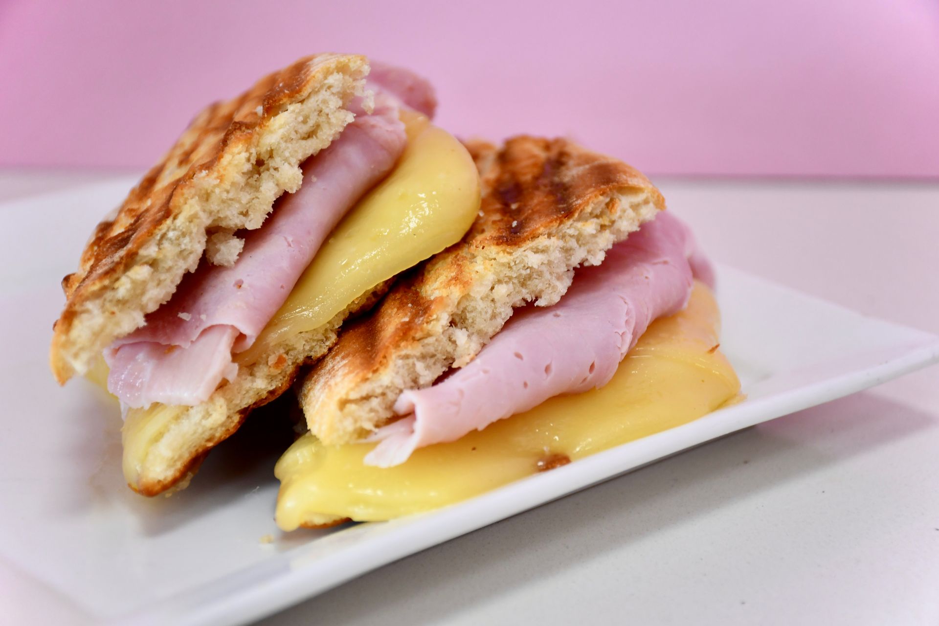 Two sandwiches with ham and cheese on a white plate