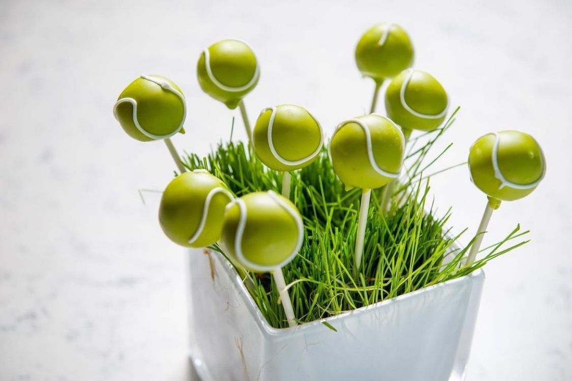A white vase filled with green tennis balls on sticks.