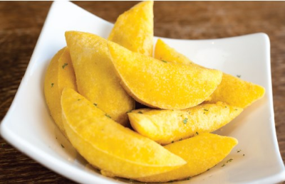 A white plate topped with yellow potato wedges on a wooden table.
