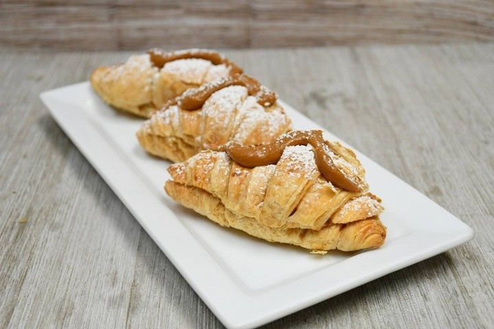 Three croissants with caramel sauce and powdered sugar on a white plate.