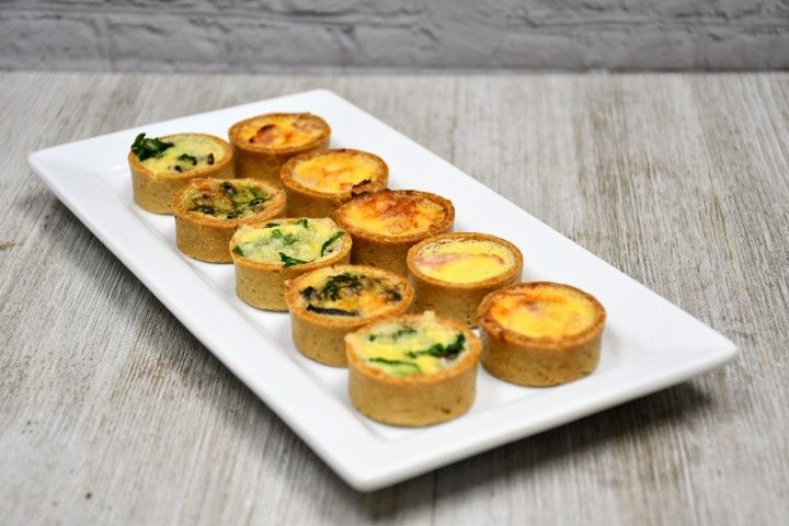A white plate topped with a variety of quiches on a wooden table.