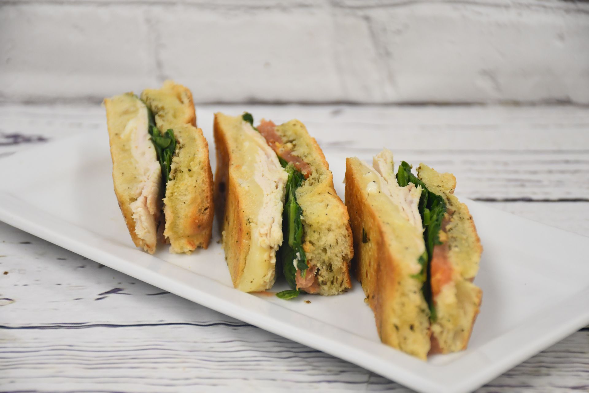 Three sandwiches are sitting on a white plate on a wooden table.