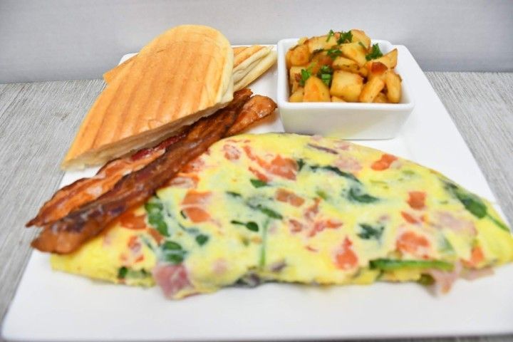 A white plate topped with an omelet , bacon , and potatoes.