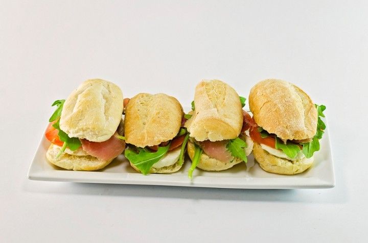 Four sandwiches are lined up on a white plate.
