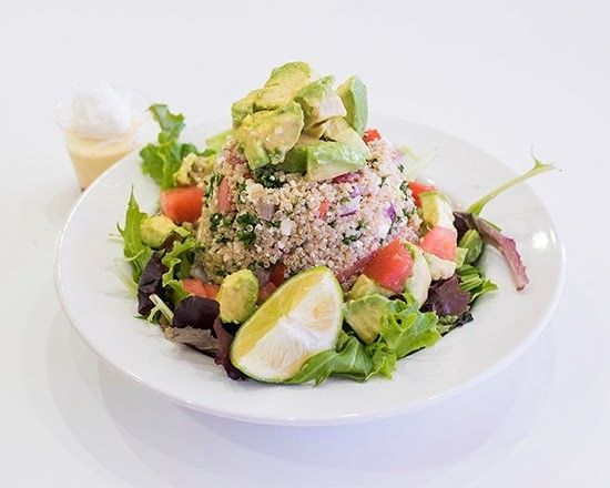 A salad with quinoa , avocado , tomatoes and lettuce on a white plate.
