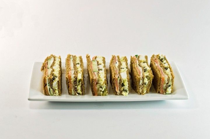 A white plate topped with a row of sandwiches on a white surface.