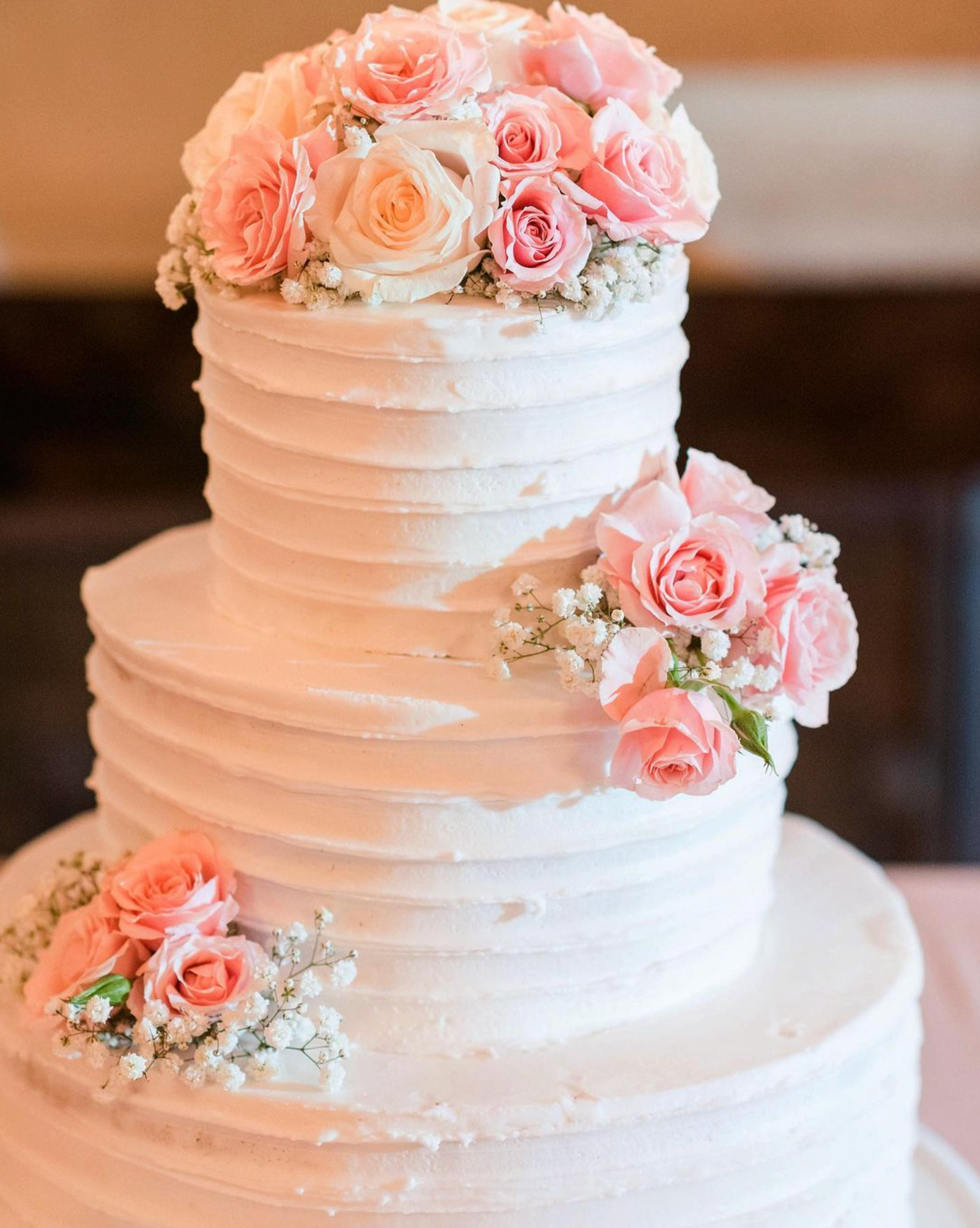 A wedding cake with pink roses and baby 's breath on top.