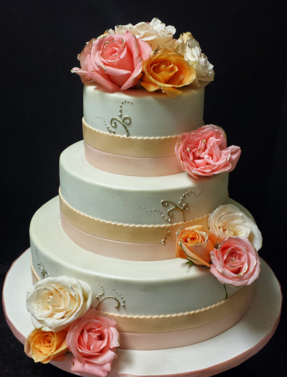 A wedding cake with pink and orange roses on top