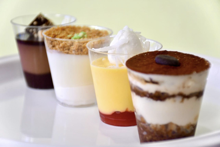 Four cups of desserts are lined up on a white plate.