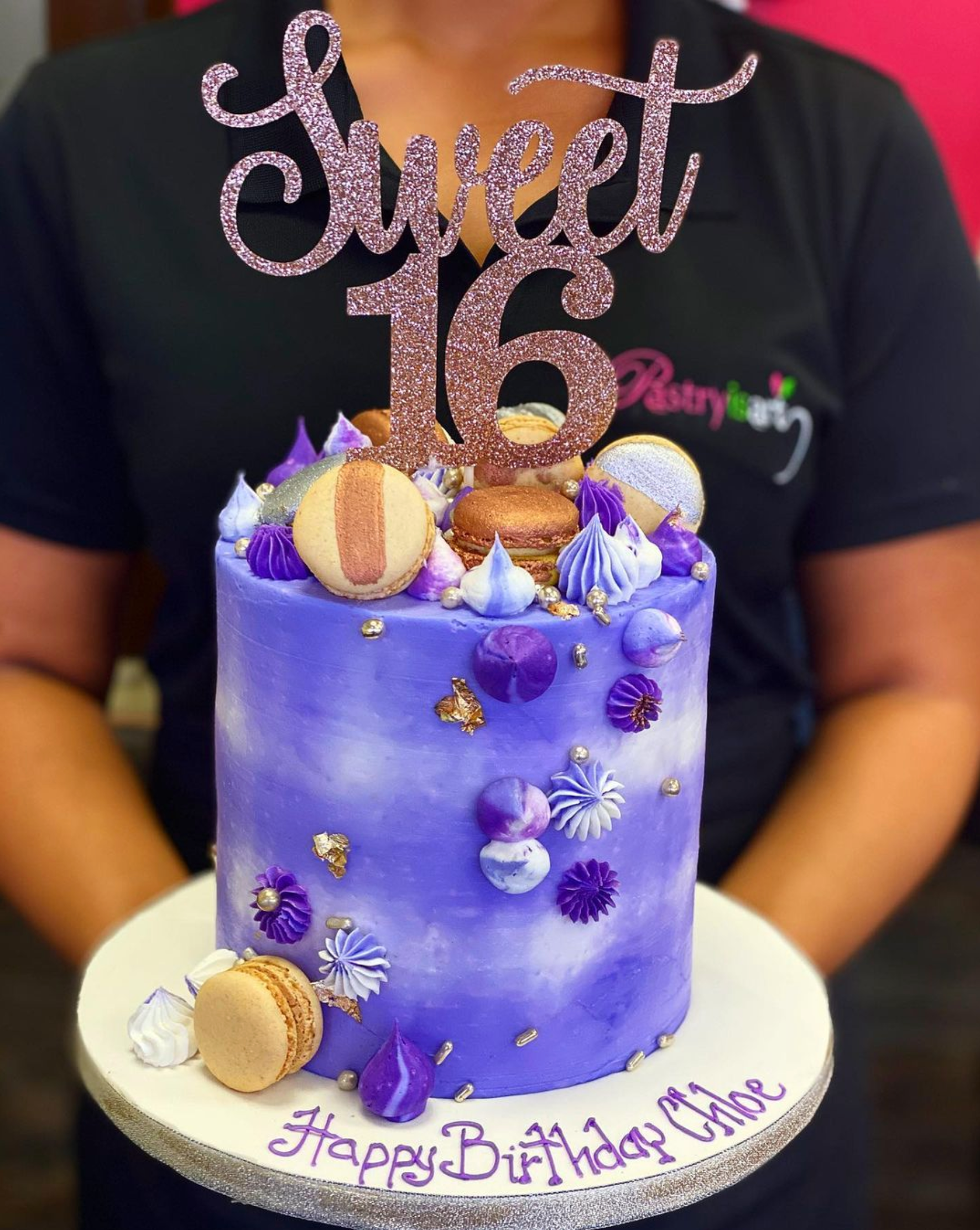 A woman is holding a purple cake with a topper that says sweet 16
