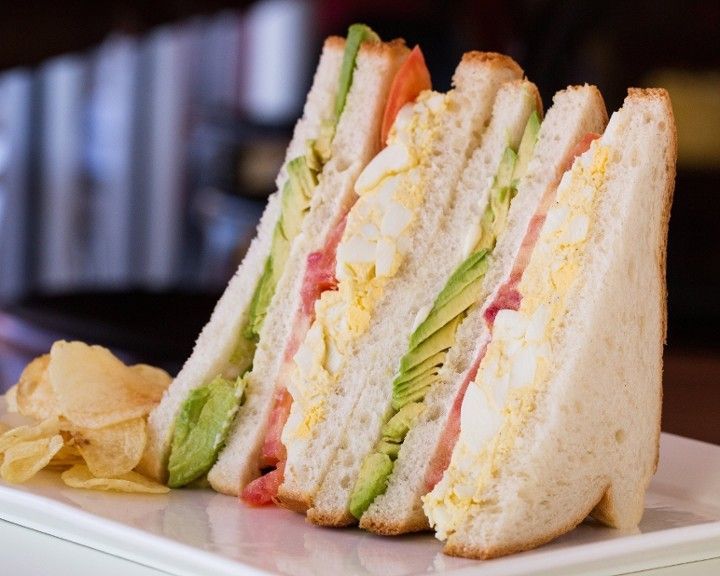 A club sandwich on a white plate with potato chips