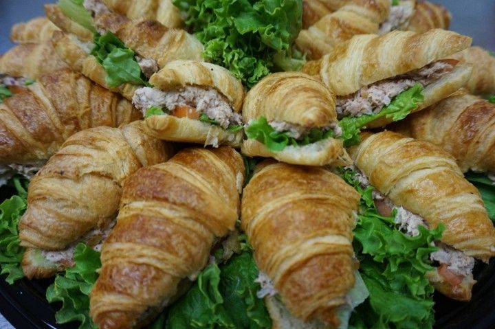 A tray of croissant sandwiches with lettuce on a table.