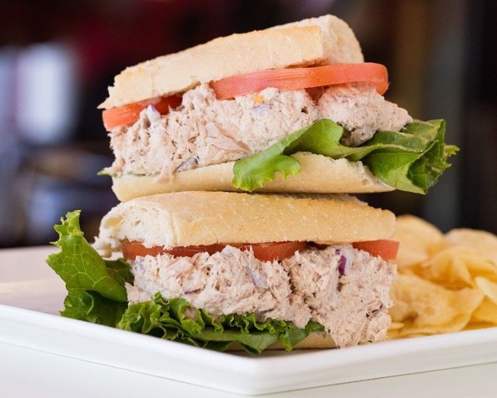 A tuna sandwich is stacked on top of another sandwich on a plate with chips.
