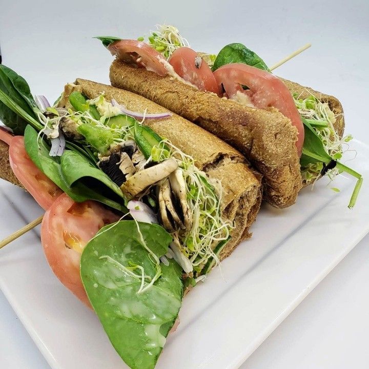 A sandwich with spinach , tomatoes and mushrooms on a white plate