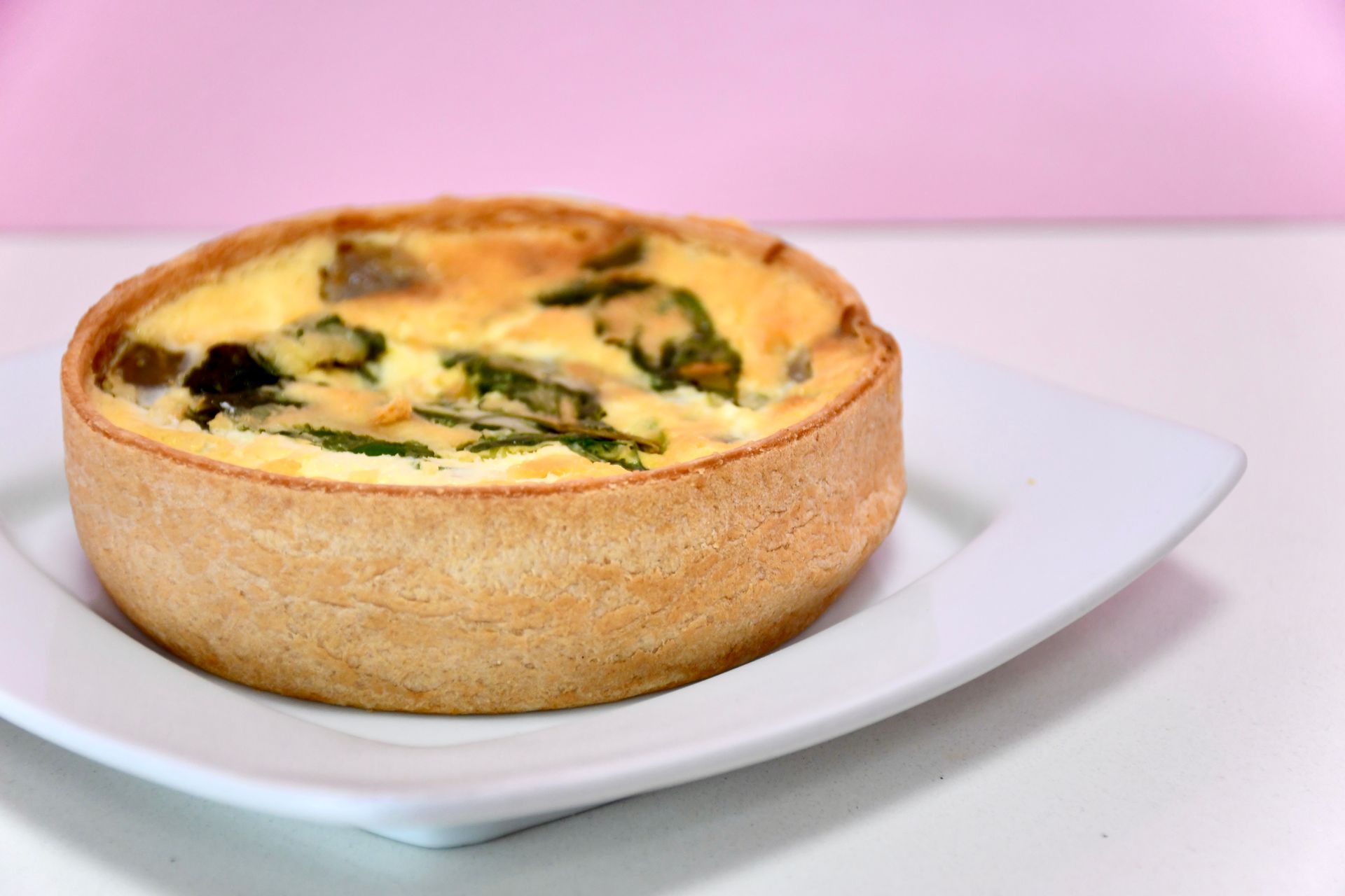 A quiche is sitting on a white plate on a table.