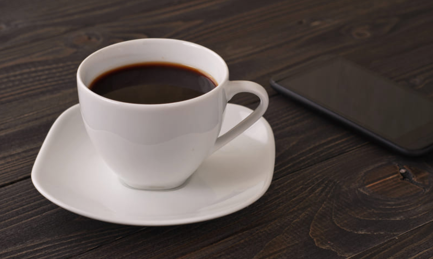 A cup of coffee on a saucer next to a tablet
