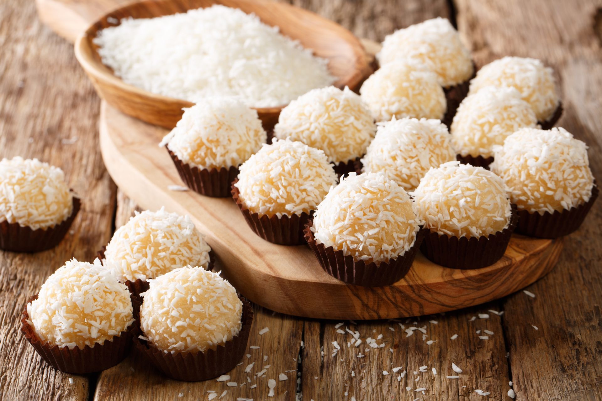 A wooden cutting board topped with coconut balls on a wooden table.