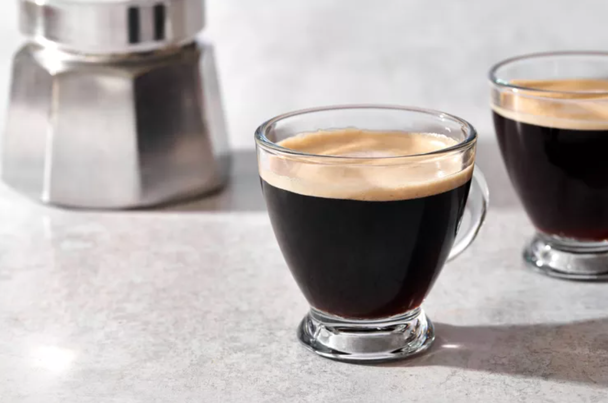 Two cups of coffee are sitting on a table next to a coffee pot.