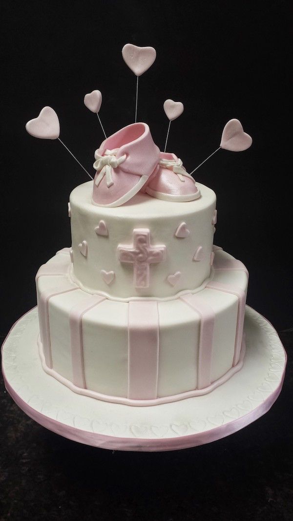 A baby shower cake with pink shoes and hearts on top.