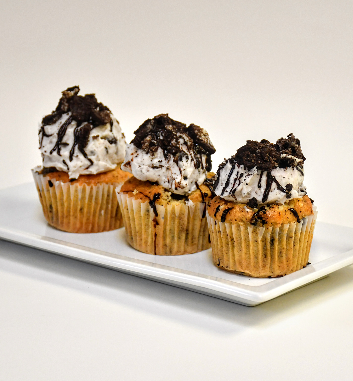 Three cupcakes on a white plate with chocolate frosting on top