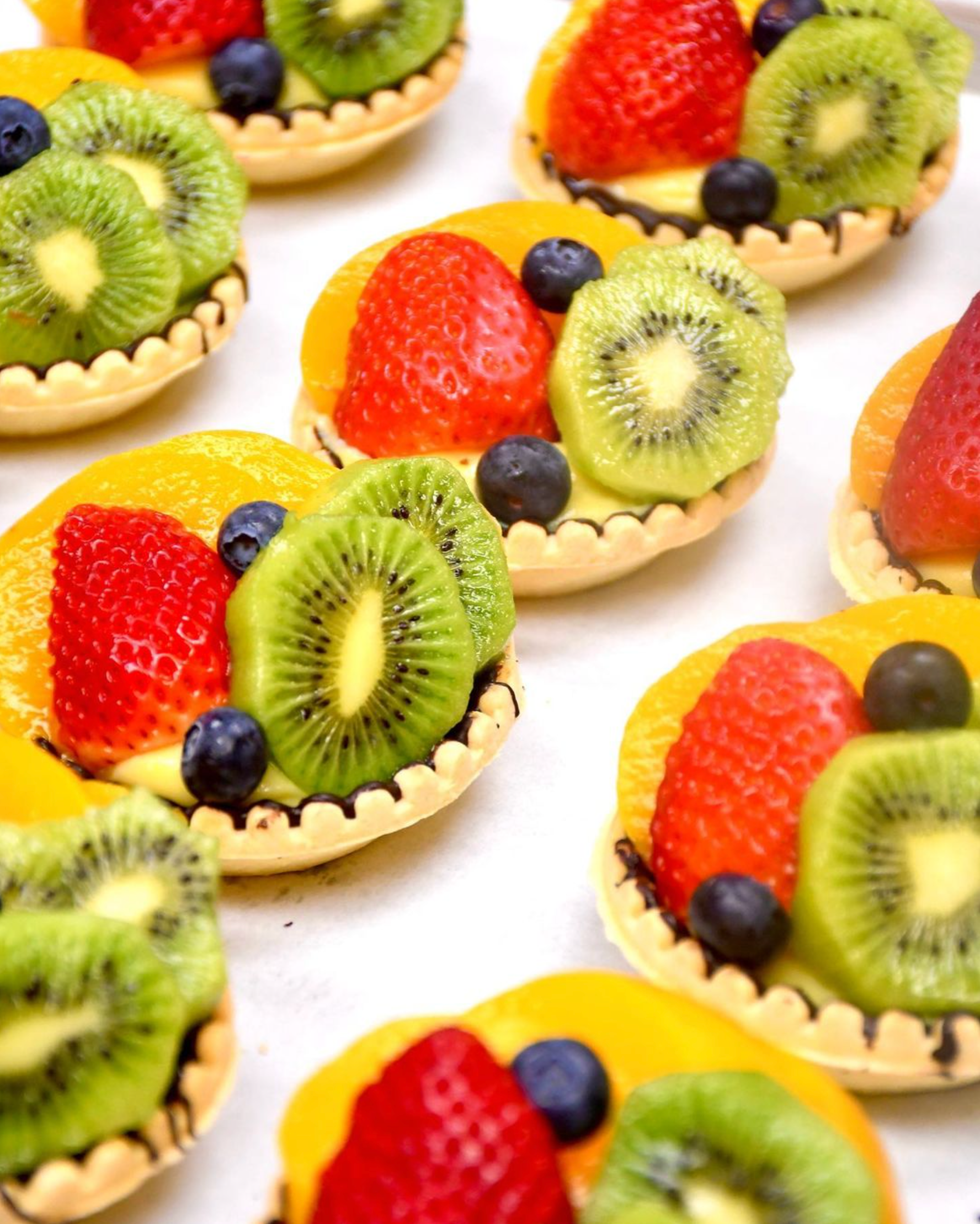 A bunch of fruit tarts with kiwi strawberries and blueberries