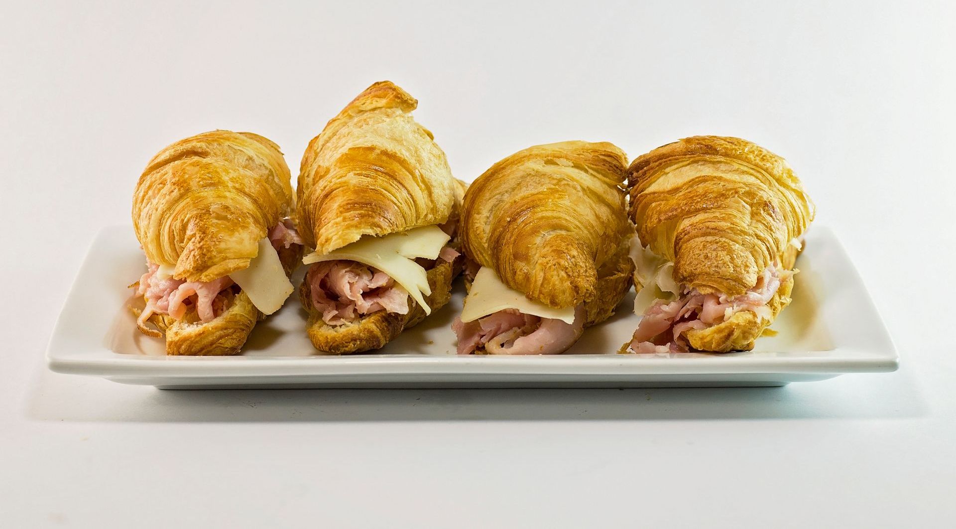 Four croissants with ham and cheese on a white plate.