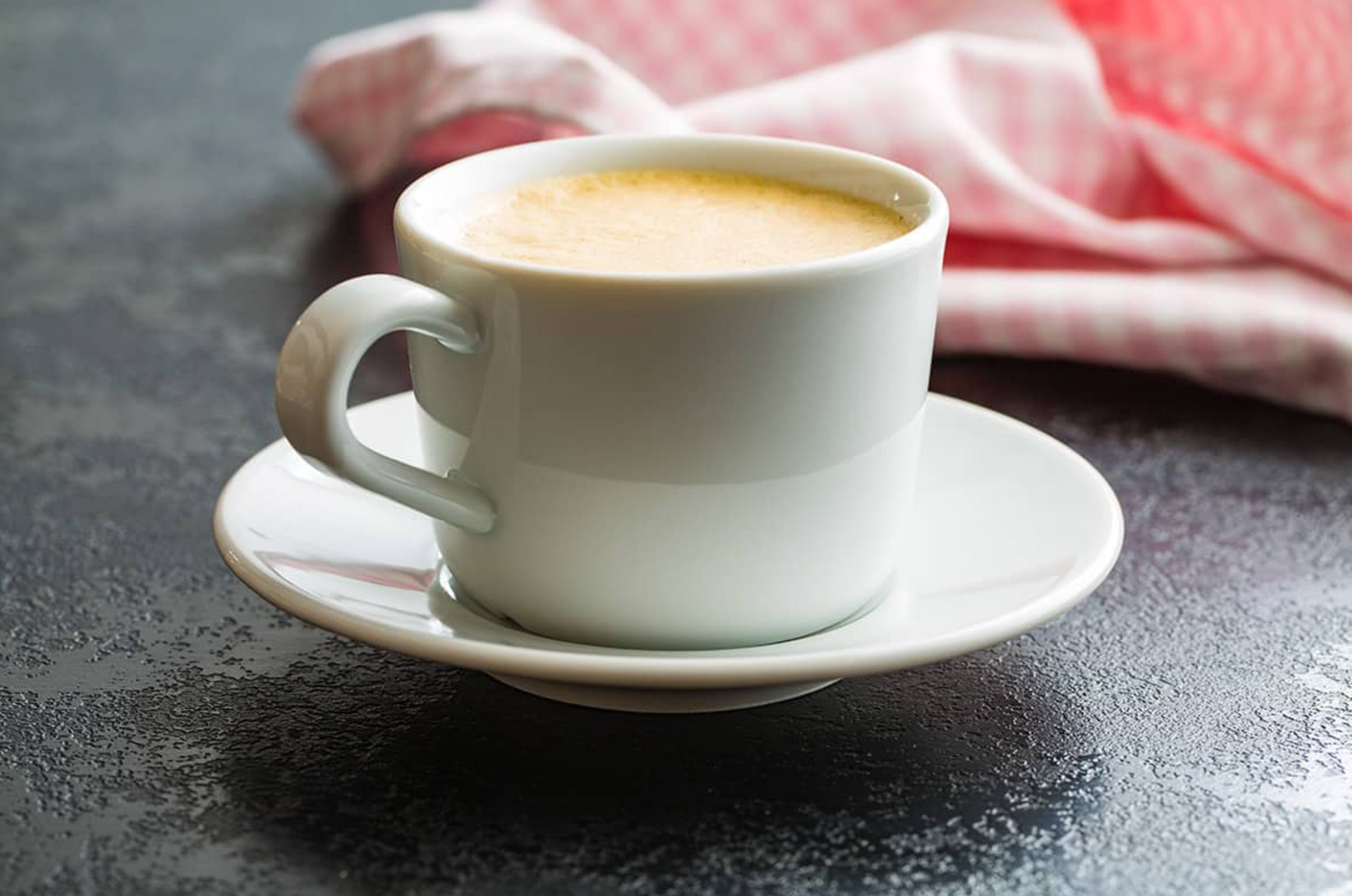 A cup of coffee is sitting on a saucer on a table.