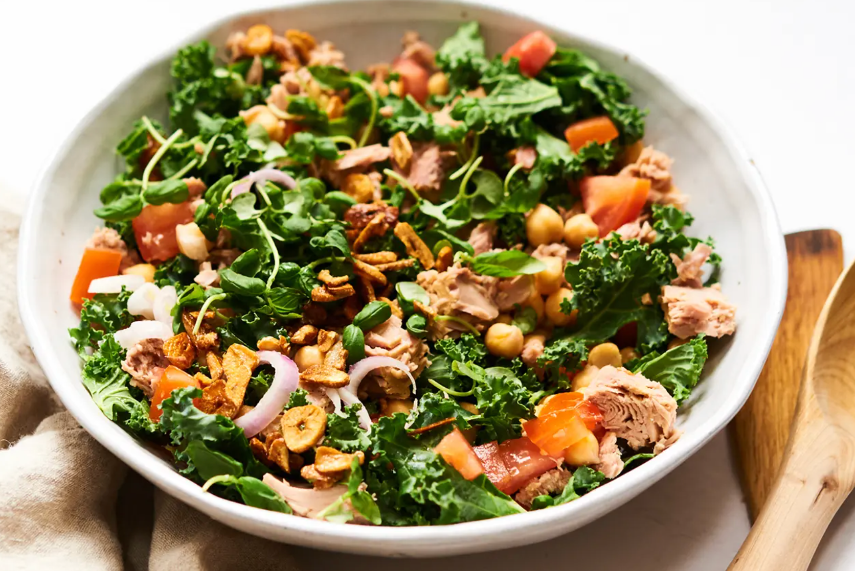 A salad with kale , chickpeas , tomatoes , onions and tuna in a white bowl.