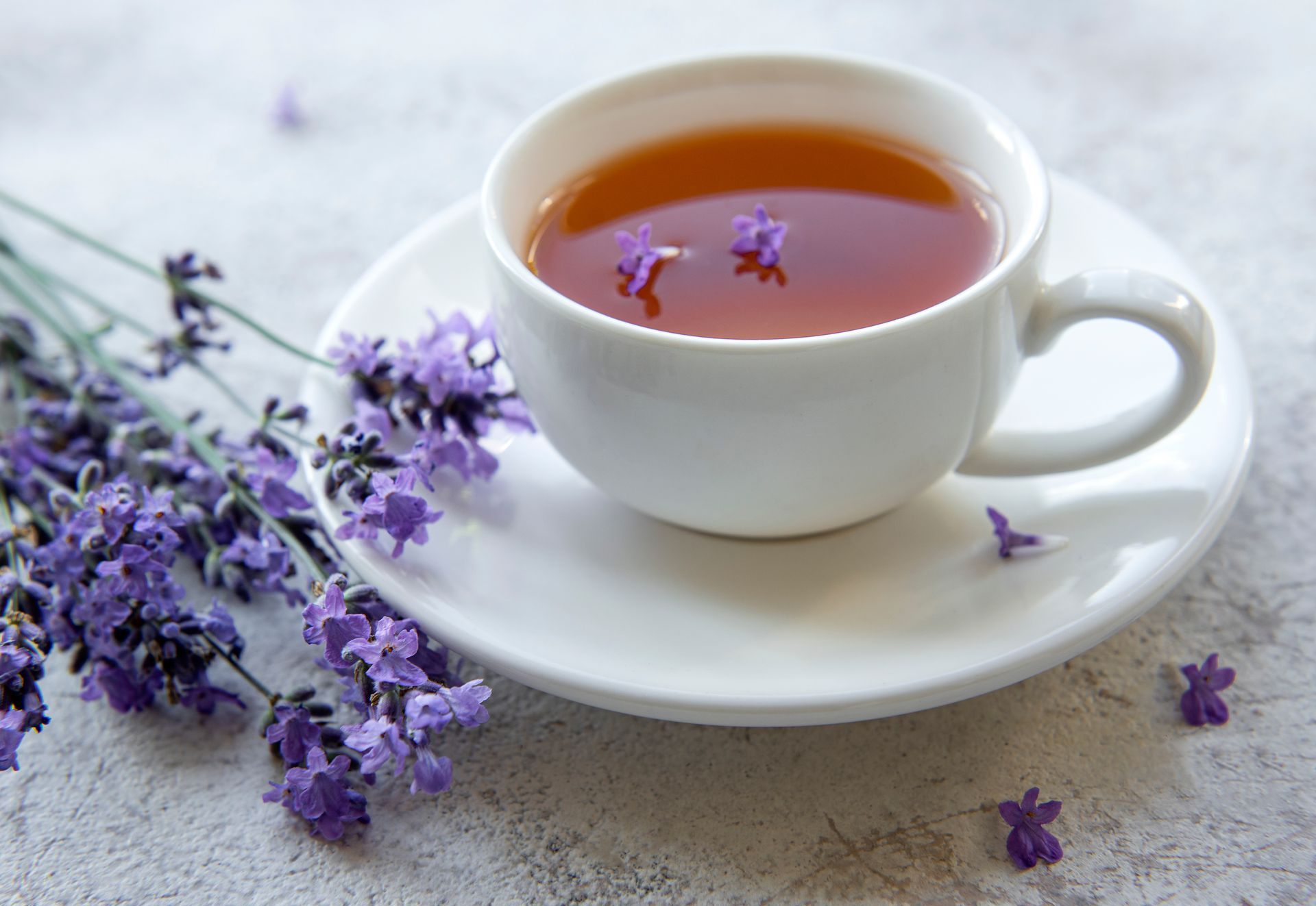 A cup of tea with purple flowers on a saucer on a table.
