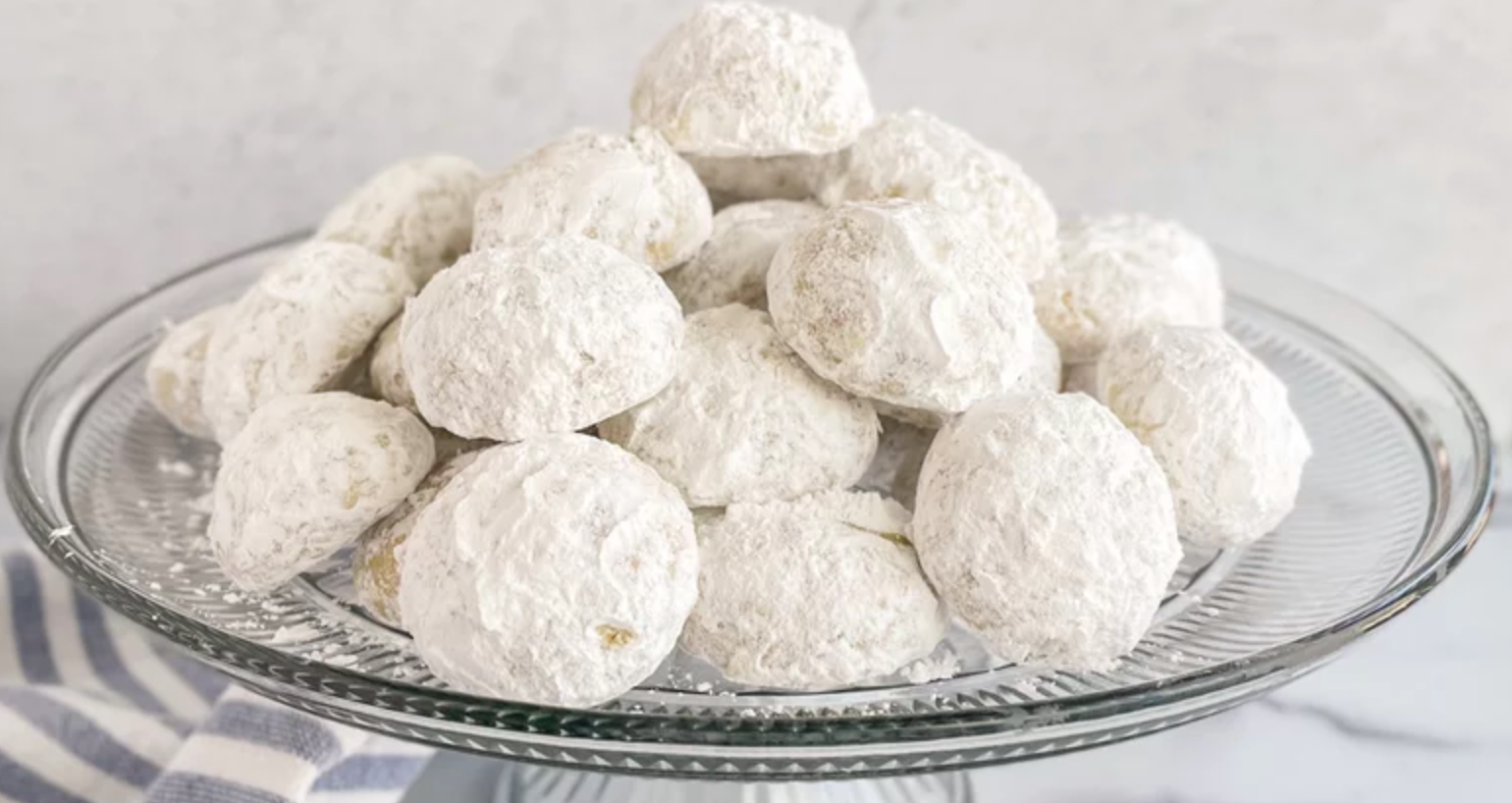 A glass plate filled with powdered sugar cookies on a table.