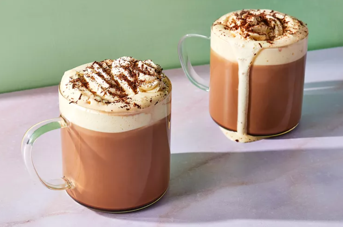Two cups of hot chocolate with whipped cream and chocolate shavings on a table.