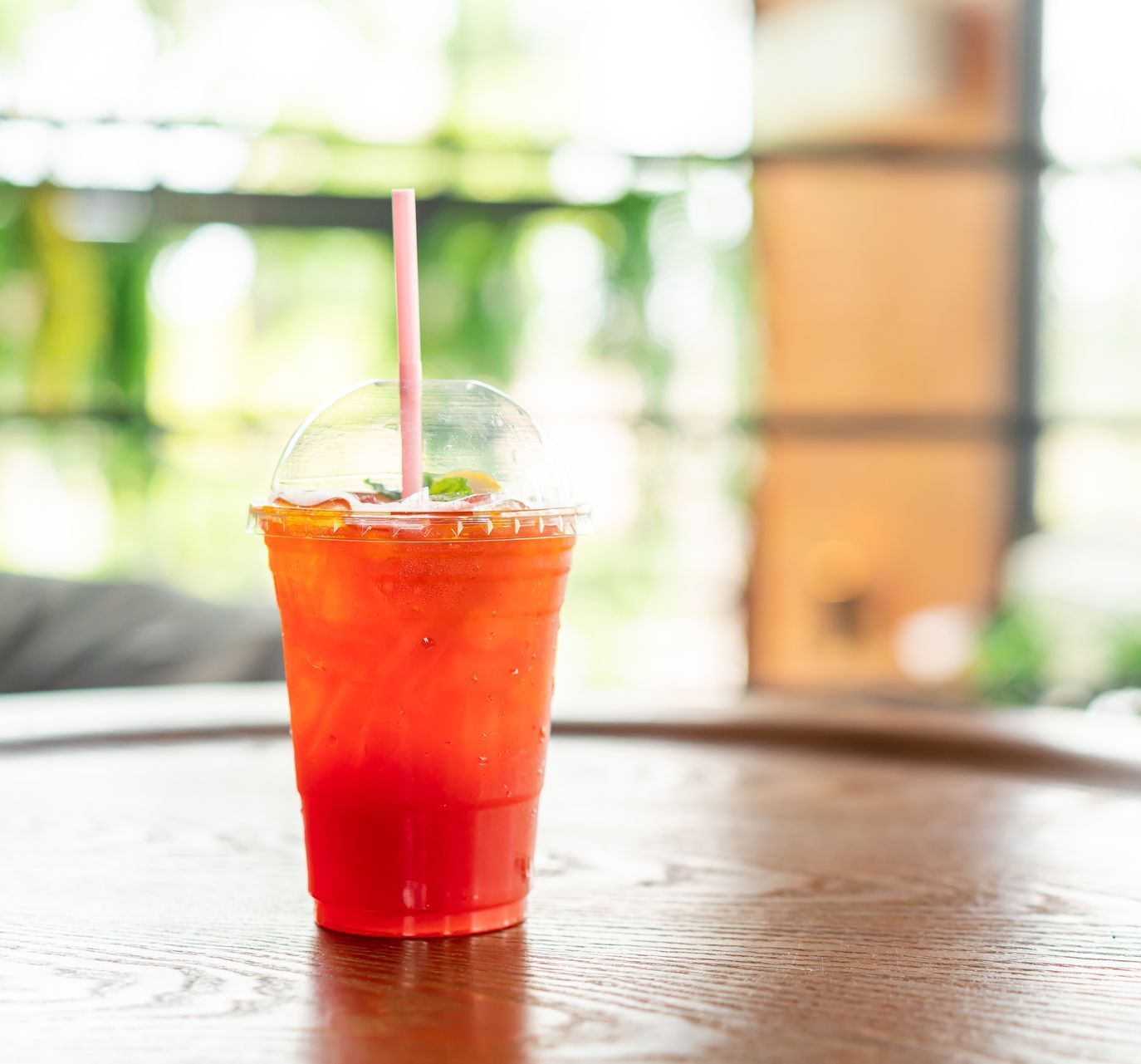 A red drink in a plastic cup with a straw on a wooden table.