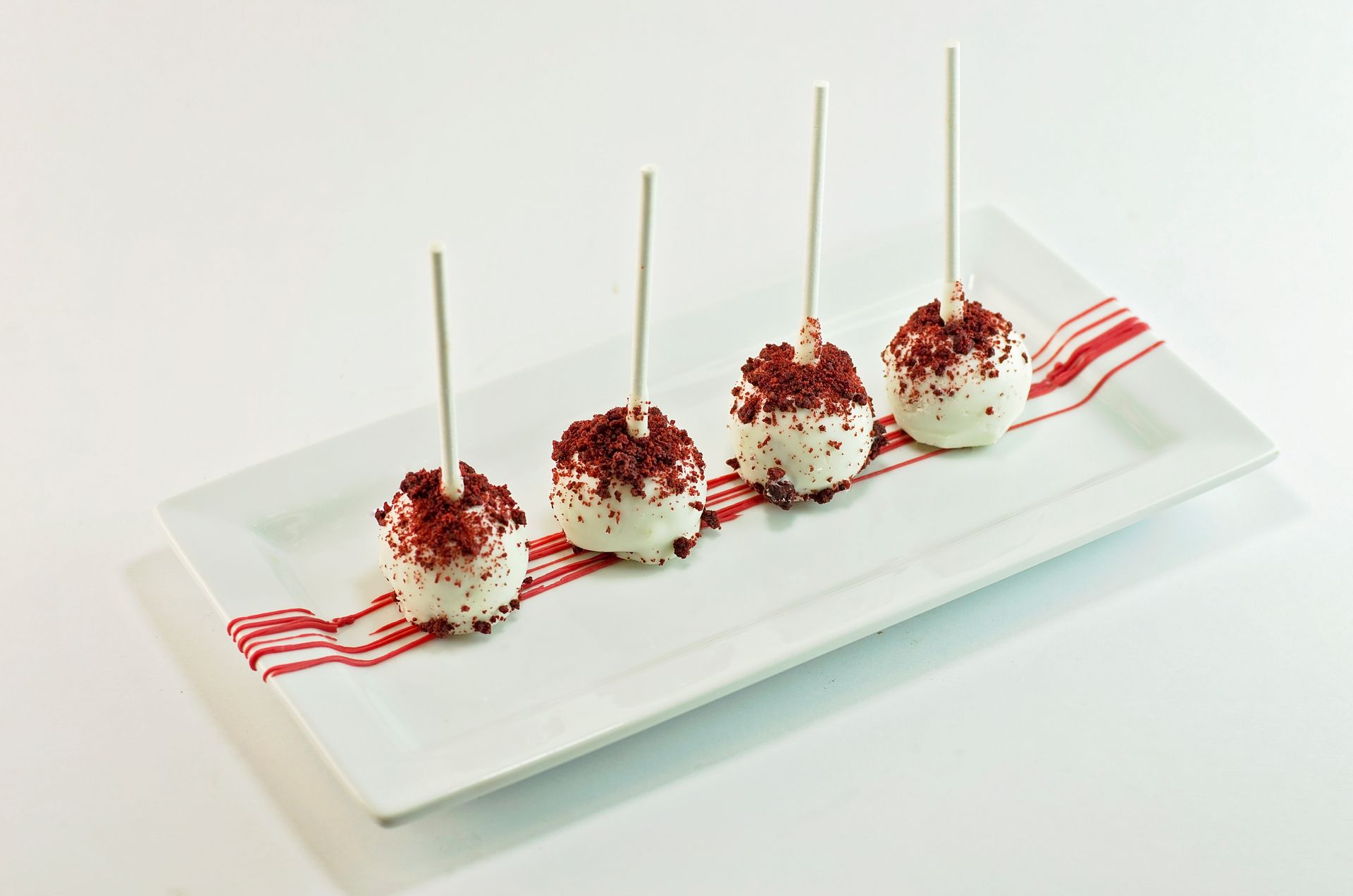 Four red velvet cake pops are on a white plate.