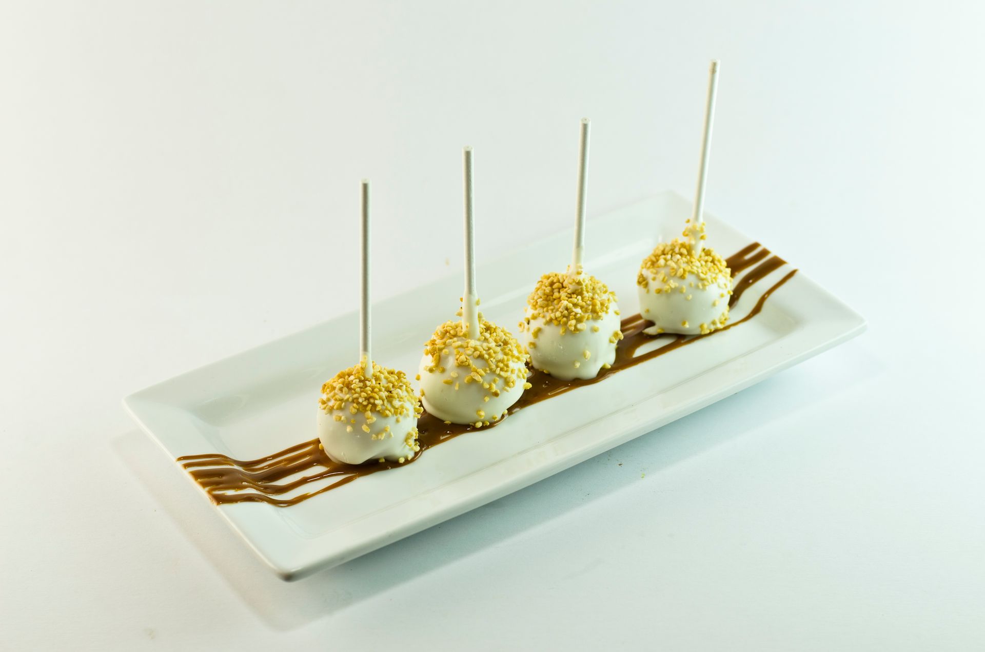 Four cake pops on a white plate with chocolate sauce