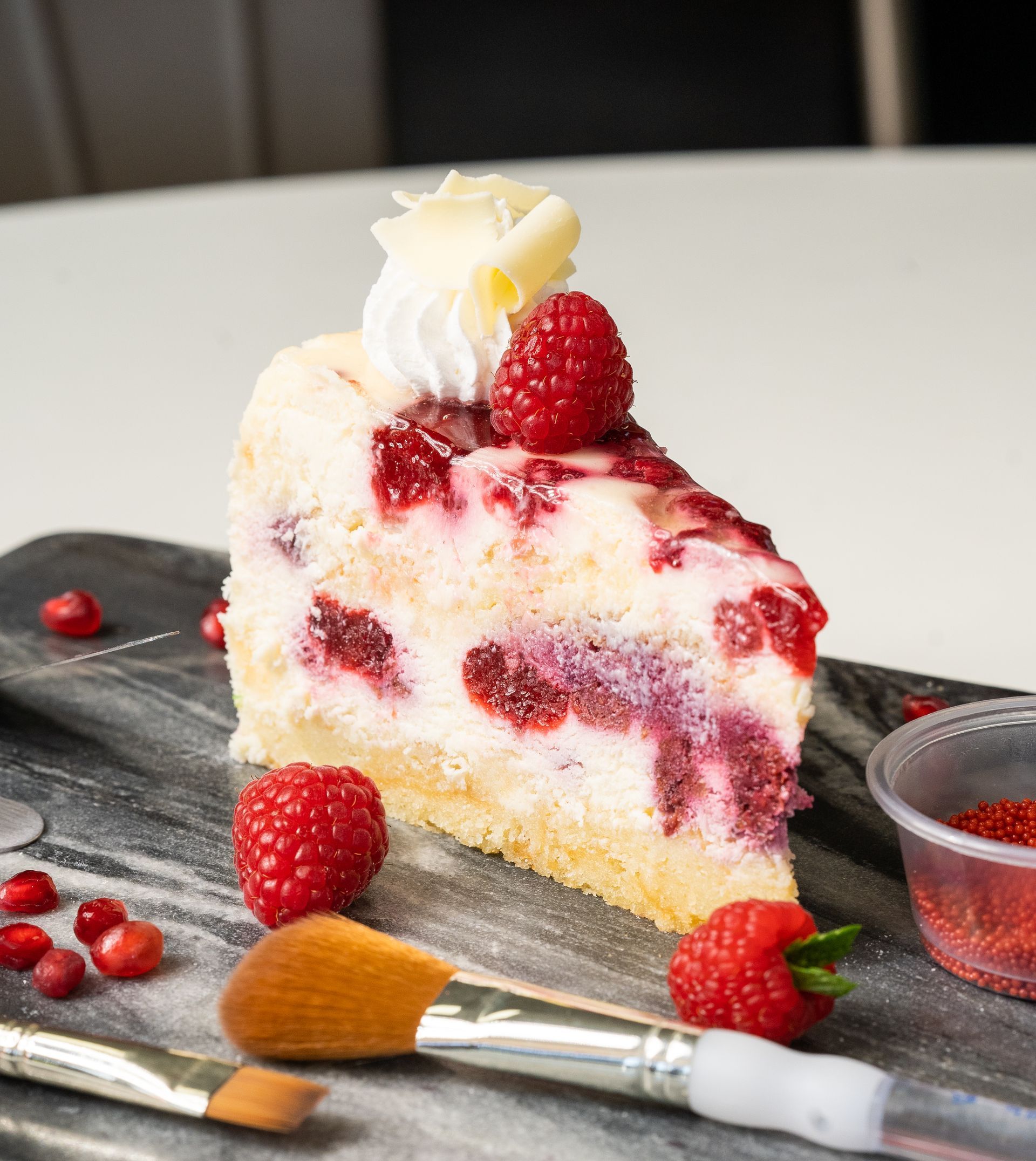 A slice of cheesecake with raspberries and whipped cream on top.
